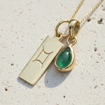 Gold necklace with a Gemini sign pendant and green emerald gemstone on a wooden surface