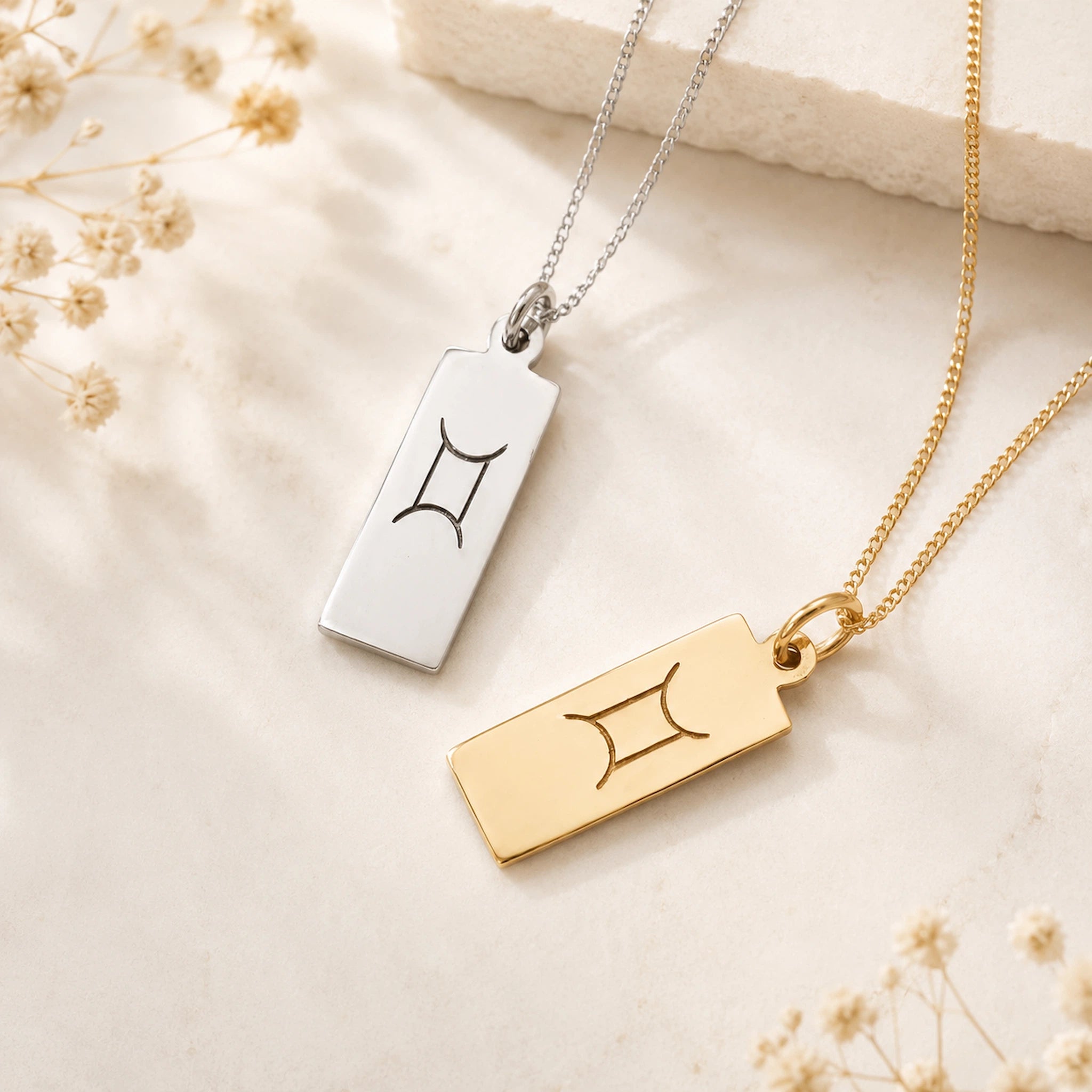 gemini necklaces flatlay featuring rectangle pendants engraved with minimalist gemini zodiac sign line glyph in sterling silver and 9k gold plated sterling silver on a light surface