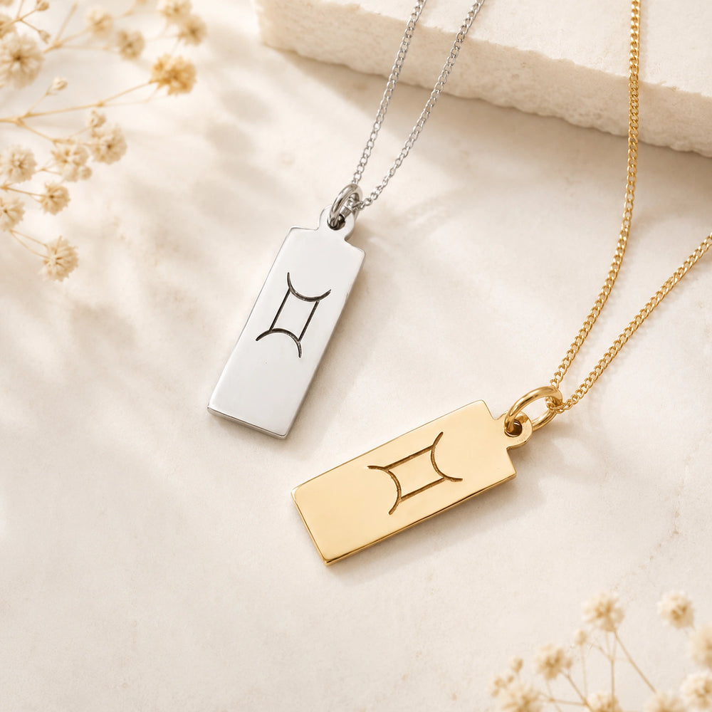 gemini necklaces flatlay featuring rectangle pendants engraved with minimalist gemini zodiac sign line glyph in sterling silver and 9k gold plated sterling silver on a light surface