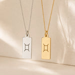 gold and sterling silver fine chain necklaces with rectangle pendants engraved with the gemini zodiac line glyph symbol hanging.