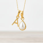 Gold necklace with 'A' pendant and teardrop-shaped pearl on a light background