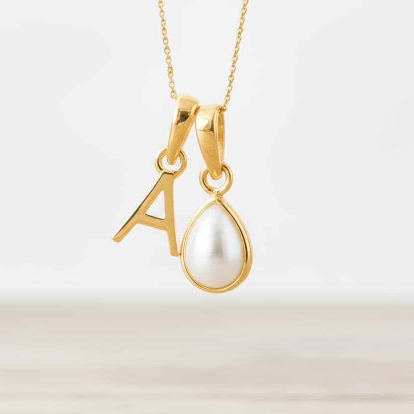 Gold necklace with 'A' pendant and teardrop-shaped pearl on a light background
