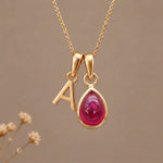 Gold Initial A Pendant and July birthstone Natural Ruby Necklace against a warm background