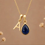 Gold Initial A Pendant and September birthstone Natural Sapphire Necklace against a warm background