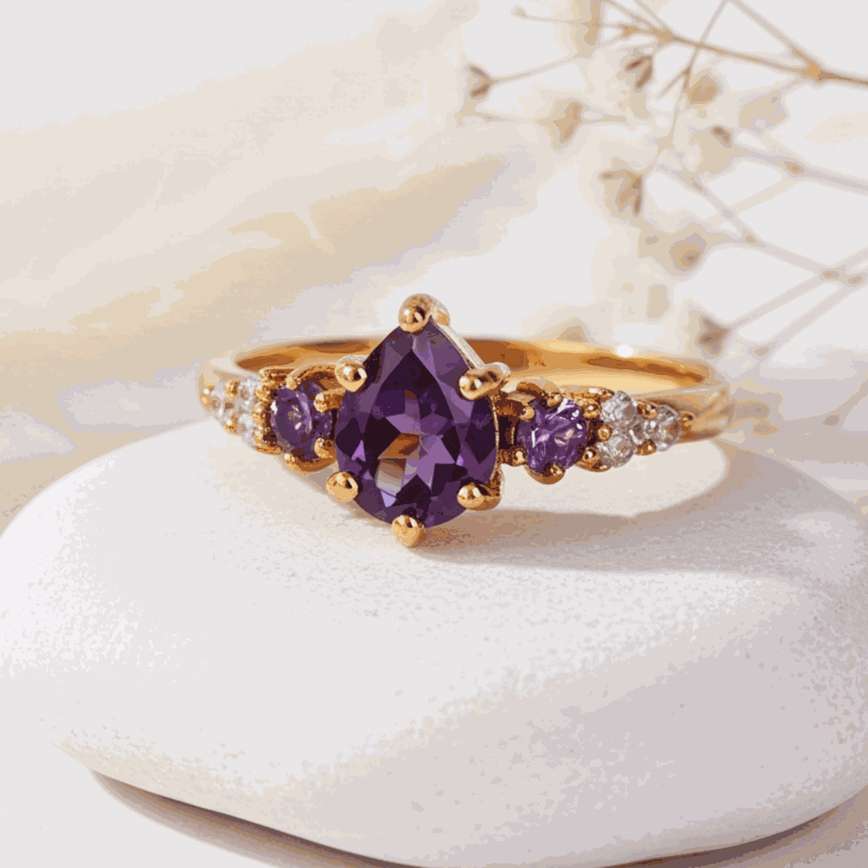 Gold ring with purple gemstones on a white stone with dried flowers in the background