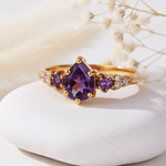 Gold ring with purple gemstones on a white stone with dried flowers in the background