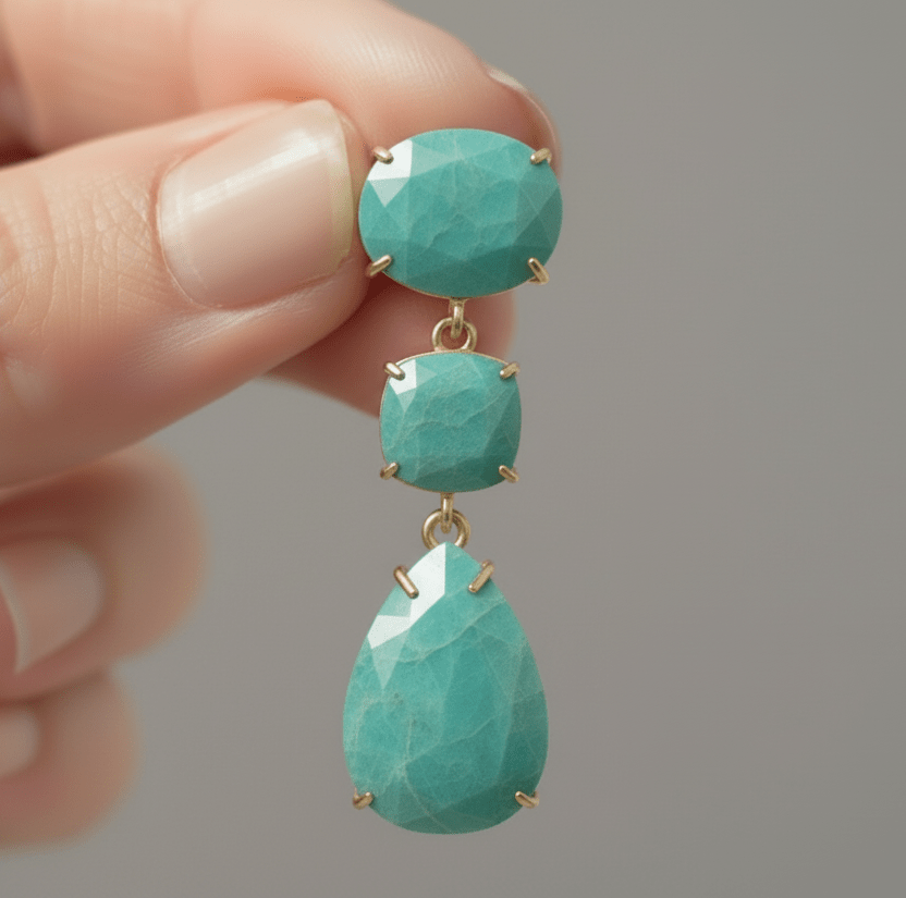Turquoise earrings with gold accents held by a hand against a blurred background