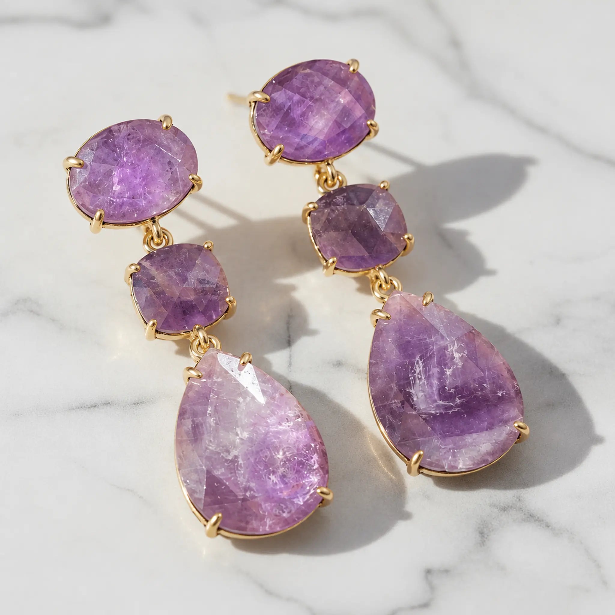 Pair of gold amethyst drop earrings on pale marble, showing the natural variations in the purple gemstones.