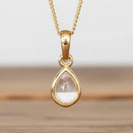 Gold april birthstone herkimer quartz necklace in tear drop shape, hanging above a wooden surface 