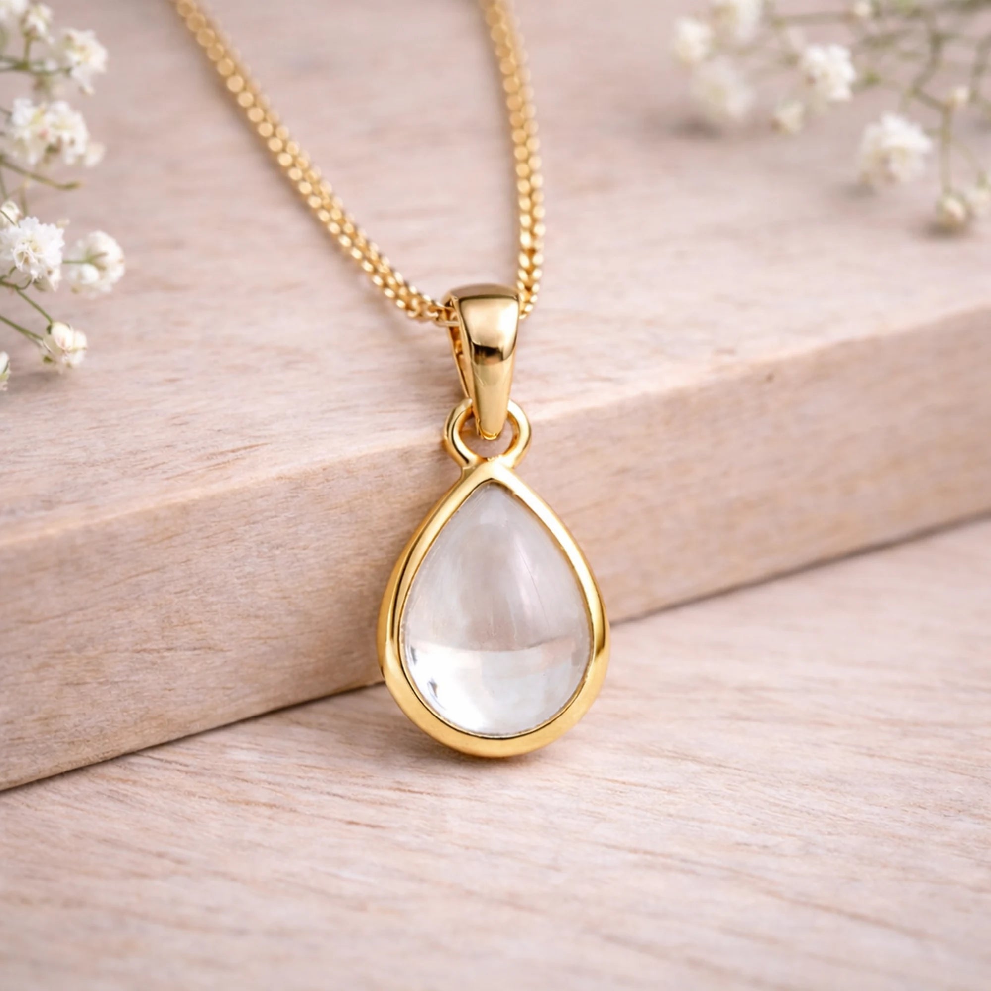 Gold necklace with a teardrop-shaped natural herkimer quartz cabochon pendant on a wooden surface