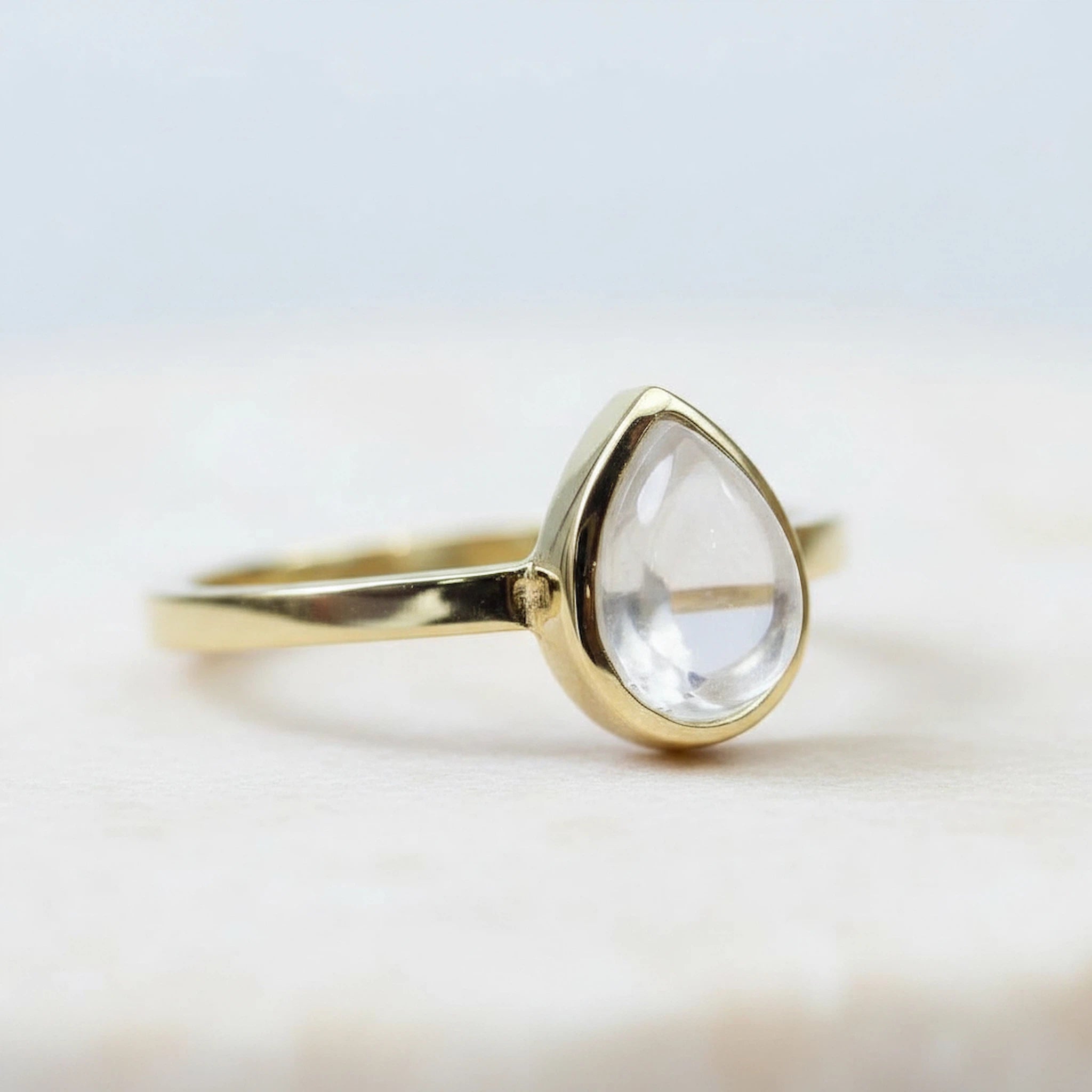 Side view of a Gold April Birthstone Ring with a teardrop-shaped natural Clear Quartz Gemstone on a white background