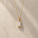 Gold fine chain necklace with a rectangle faceted bezel set april cubic zirconia pendant on a light stone background.