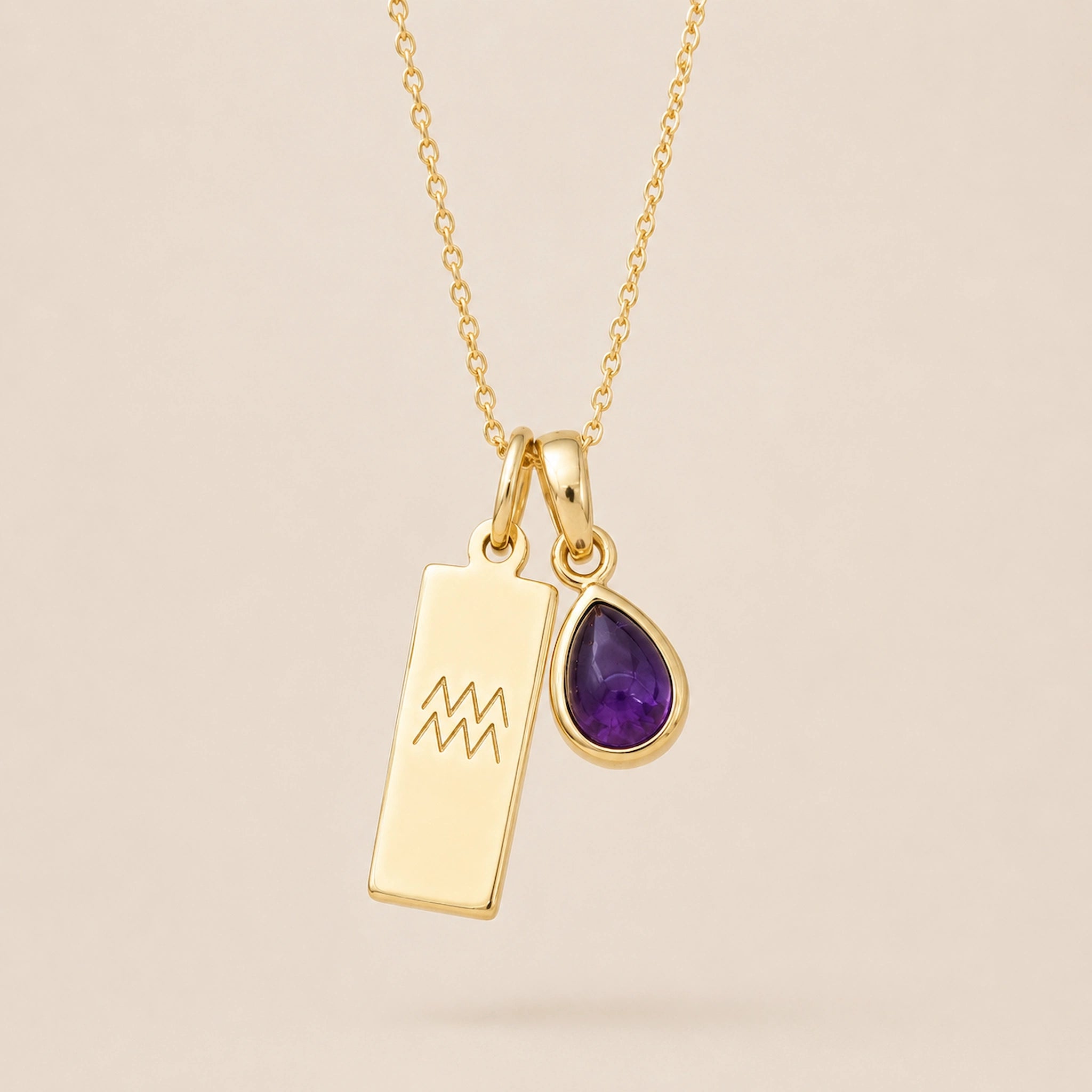 Gold necklace with a teardrop february birthstone natural amethyst pendant and engraved aquarius glyph tag hanging on a beige background.