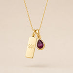 Gold necklace with a teardrop january birthstone natural garnet pendant and engraved aquarius glyph tag hanging on a beige background.