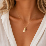Gold necklace with a teardrop january birthstone natural garnet pendant and engraved aquarius glyph tag on a person wearing a white shirt.