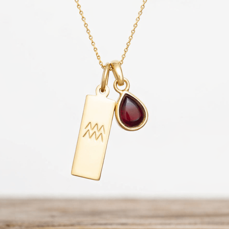 Gold necklace with a pendant featuring a gemstone and zodiac symbol on a light background