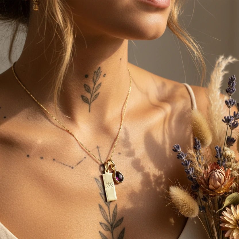 Woman wearing a gold necklace with a pendant, holding dried flowers, with tattoos on her neck.