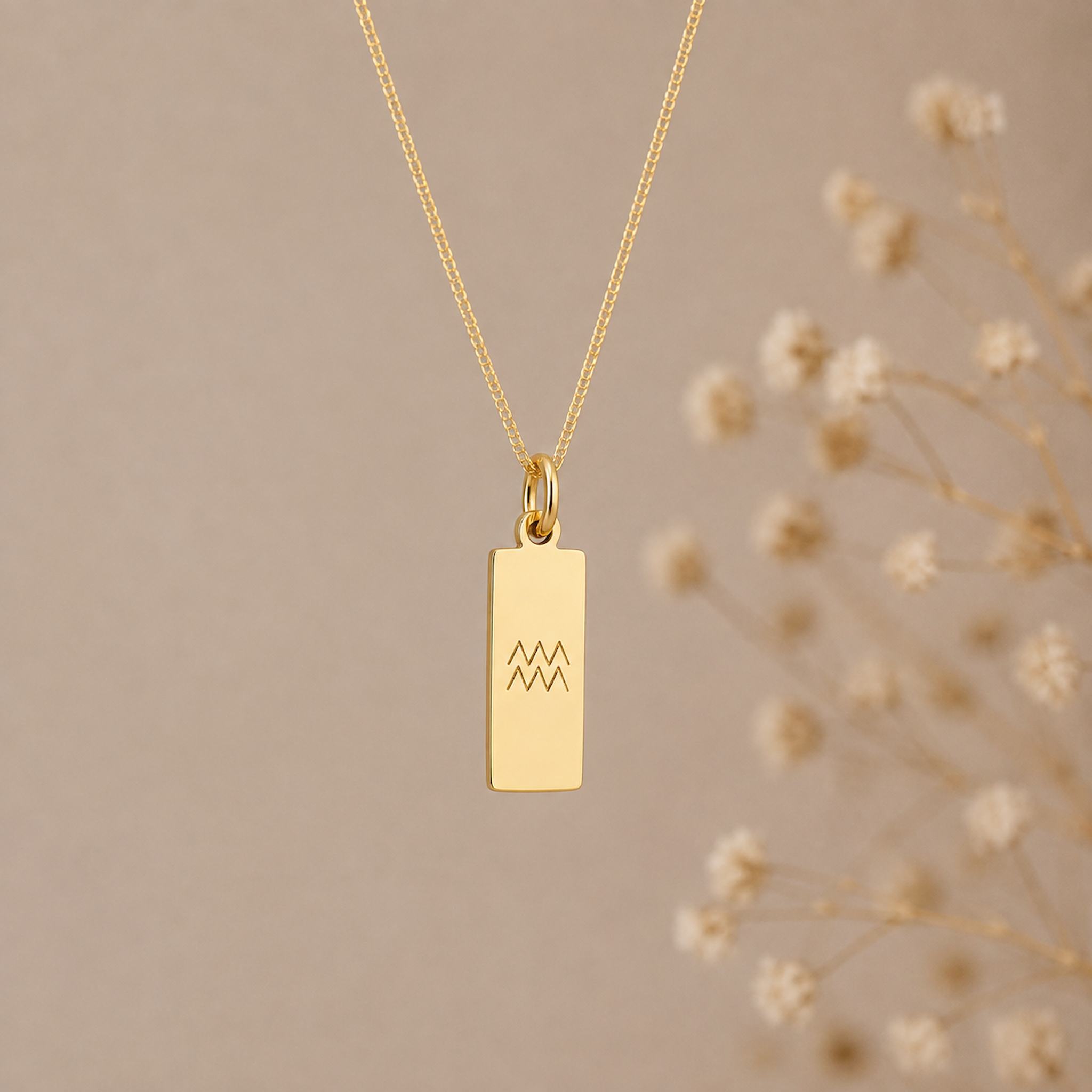 aquarius necklace - A gold rectangular pendant necklace with a simple engraved aquarius star sign line glyph symbol, hanging against a warm beige background 