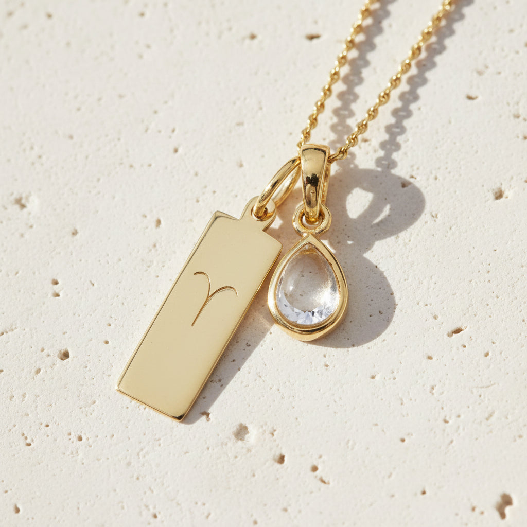 Gold necklace with Aries star sign pendant and april Birthstone herkimer quartz pendant on a stone surface