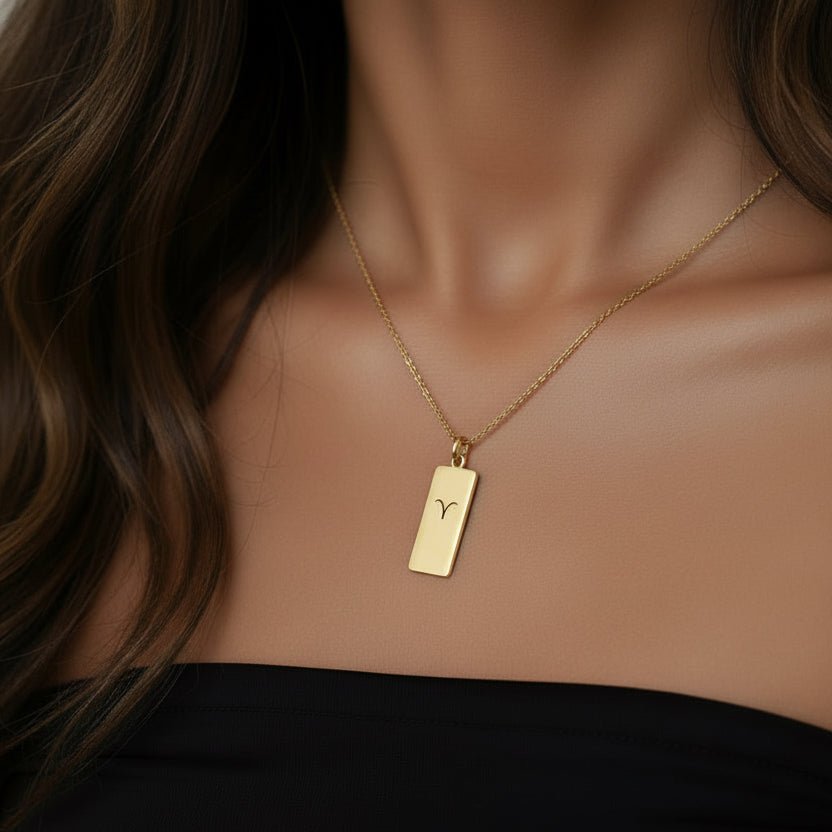Gold necklace with a rectangular pendant on a person wearing a black top.