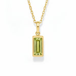 gold august birthstone necklace with light green cubic zirconia on a white background.