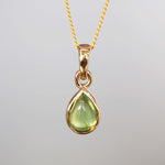 Gold pendant with a green peridot teardrop-shaped gemstone on a gray background