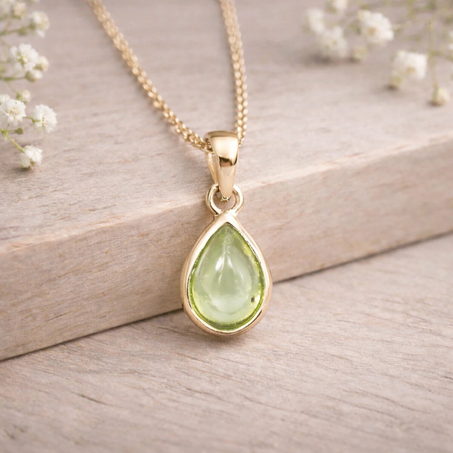 Gold august birthstone necklace with a natural period teardrop pendant on a wooden surface 