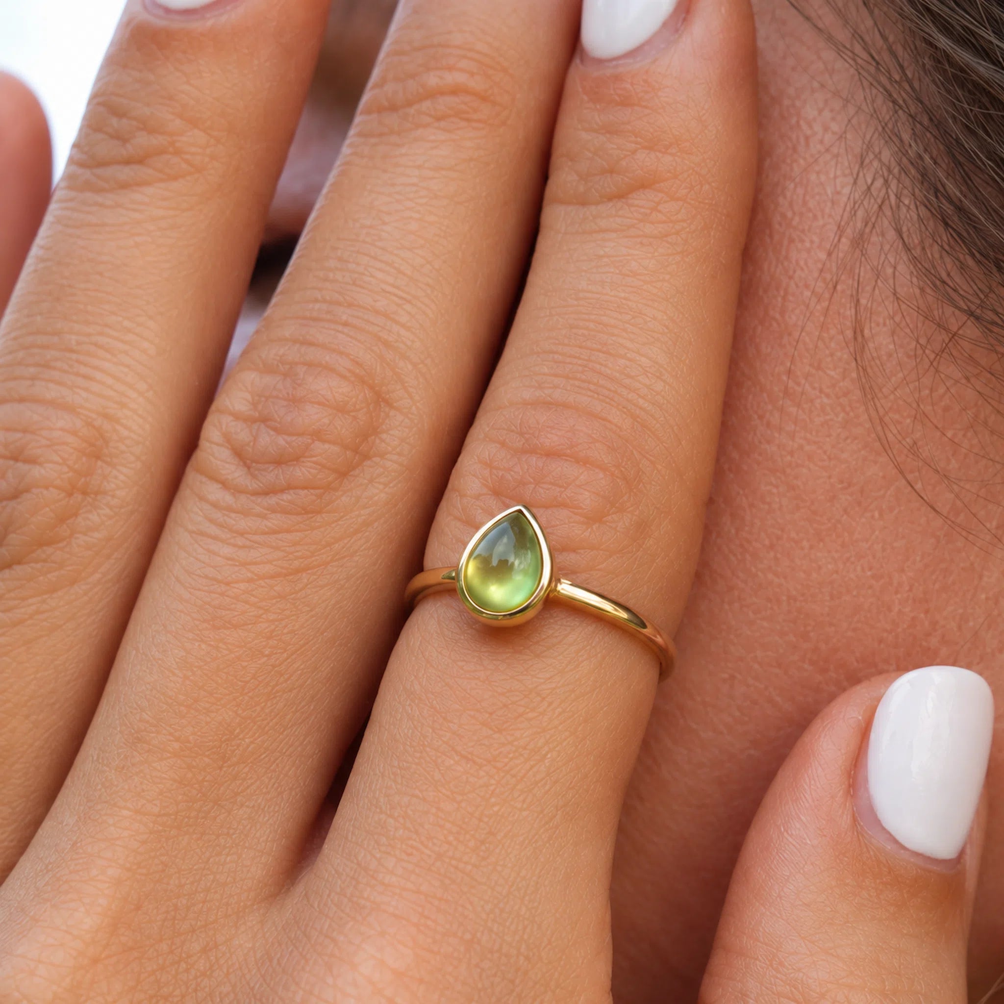 close up on a finger wearing a gold august birthstone ring featuring a pear-shaped cabochon bezel set natural peridot gemstone