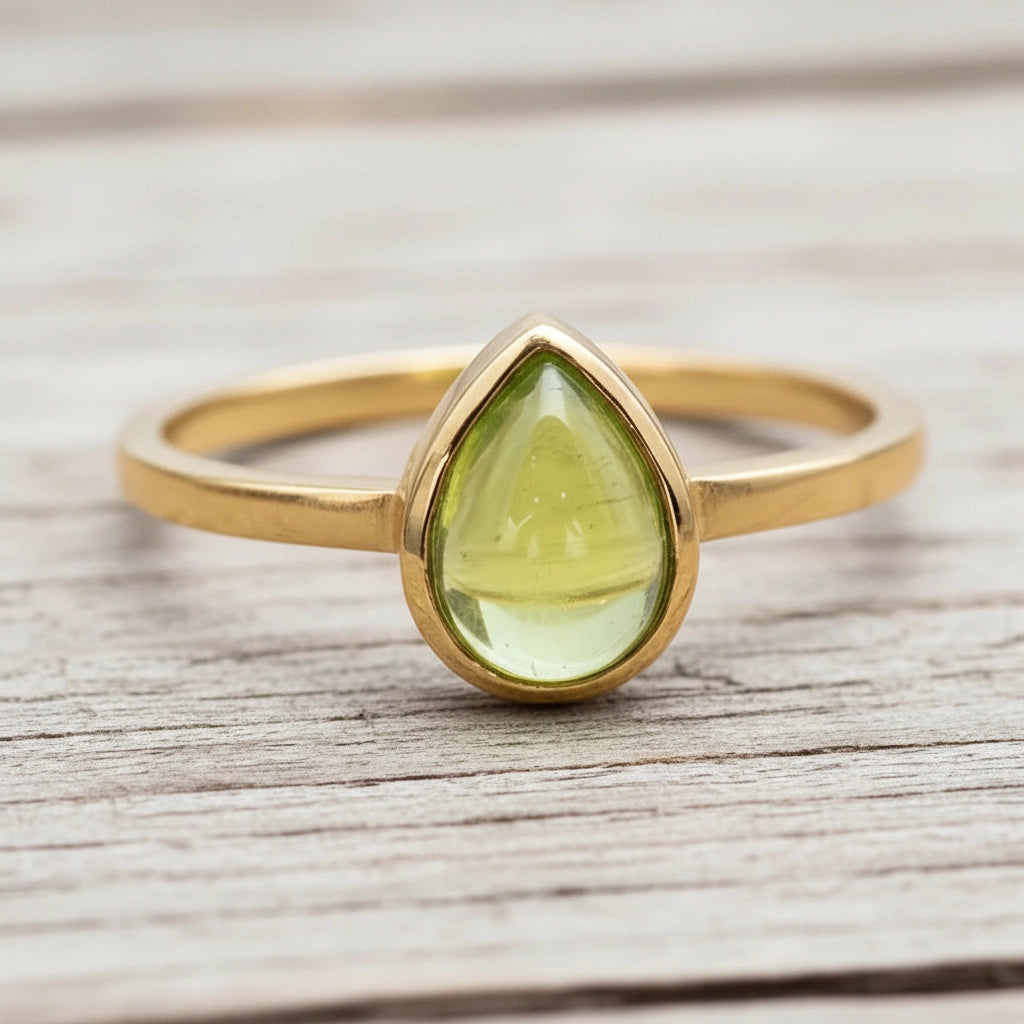 Gold ring with a green peridot teardrop-shaped gemstone on a wooden surface
