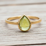 Gold ring with a green peridot teardrop-shaped gemstone on a wooden surface