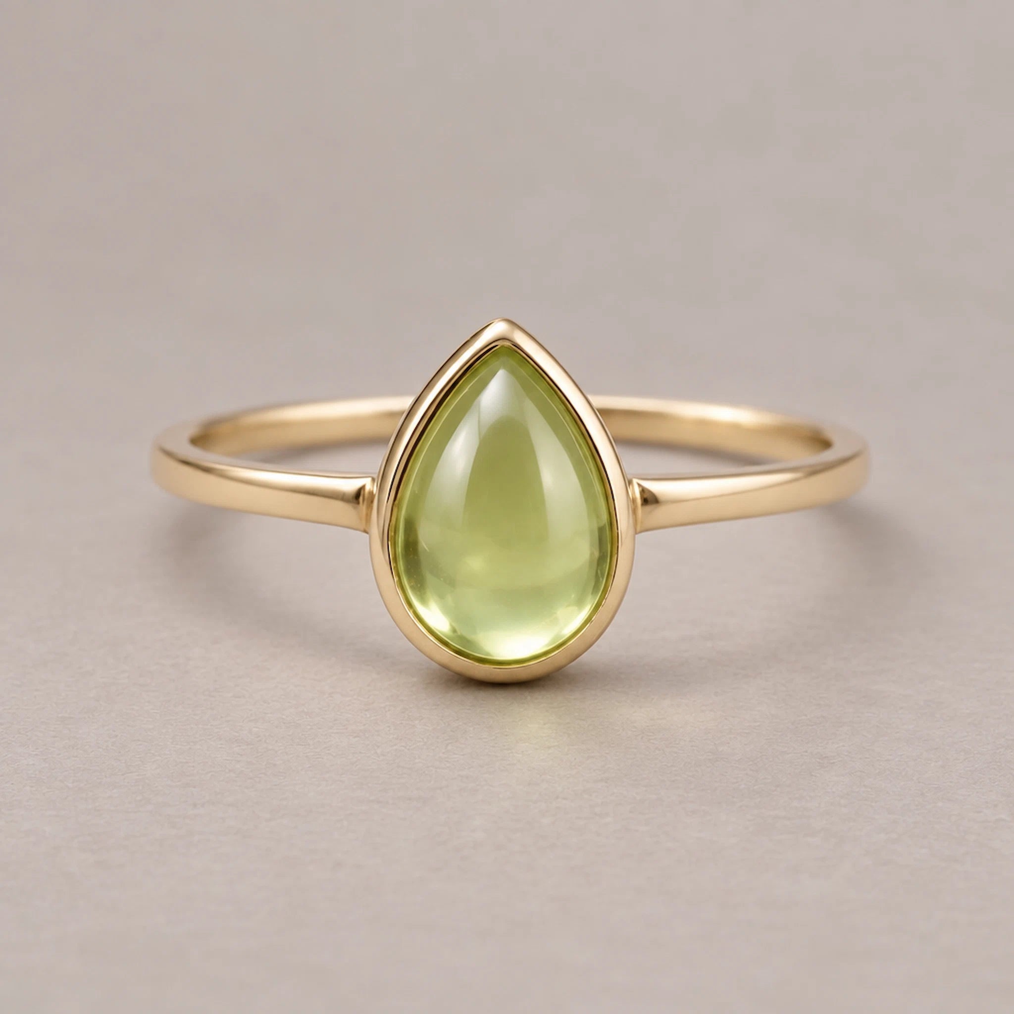 Gold august birthstone ring with a teardrop-shaped green natural peridot gemstone on a light background