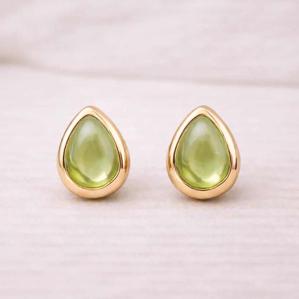 Gold august birthstone stud earrings with green teardrop natural peridot stones on a light background
