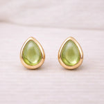 Gold earrings with green teardrop natural peridot stones on a light background