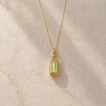 Gold fine chain necklace with a rectangle faceted bezel set august cubic zirconia pendant on a light stone background.