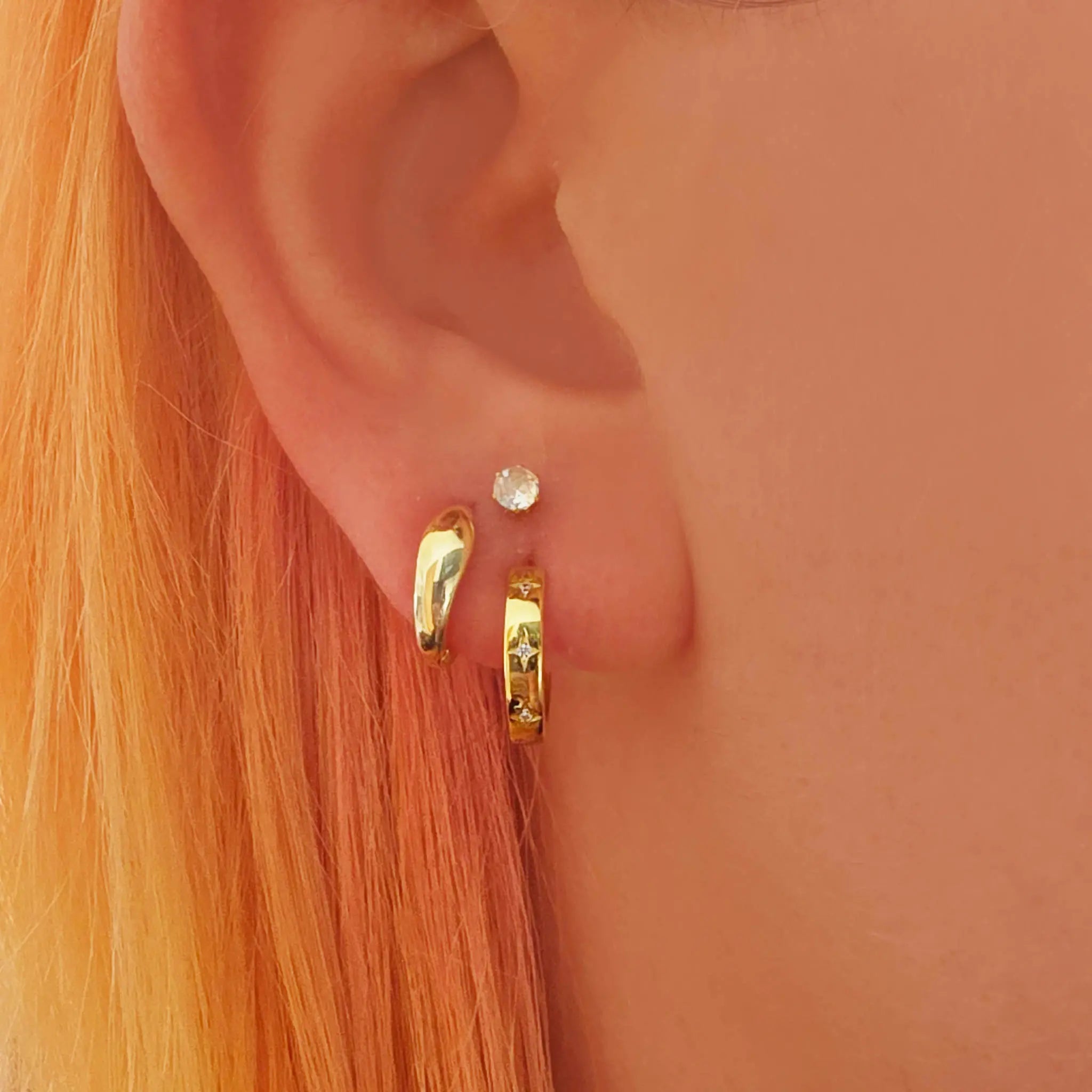 Close-up of an ear wearing gold hoop earrings with a small diamond stud
