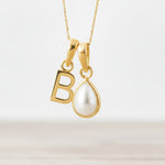 Gold necklace with a 'B' pendant and a teardrop-shaped pearl on a light background