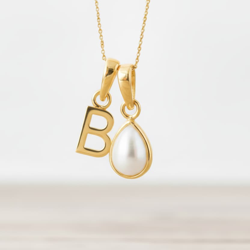 Gold necklace with a 'B' pendant and a teardrop-shaped pearl on a light background