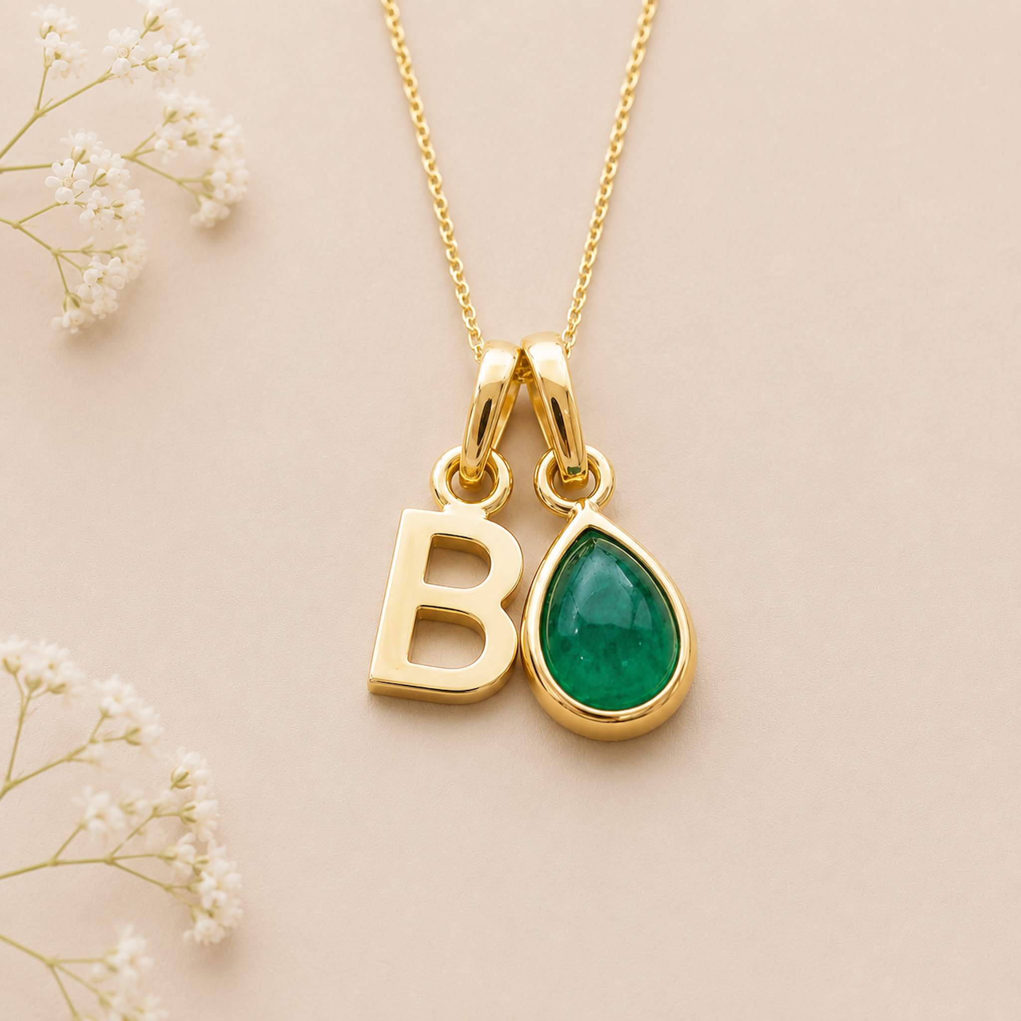 Gold May birthstone necklace with a pear-shaped natural emerald gemstone pendant and letter 'B' charm on a light background.