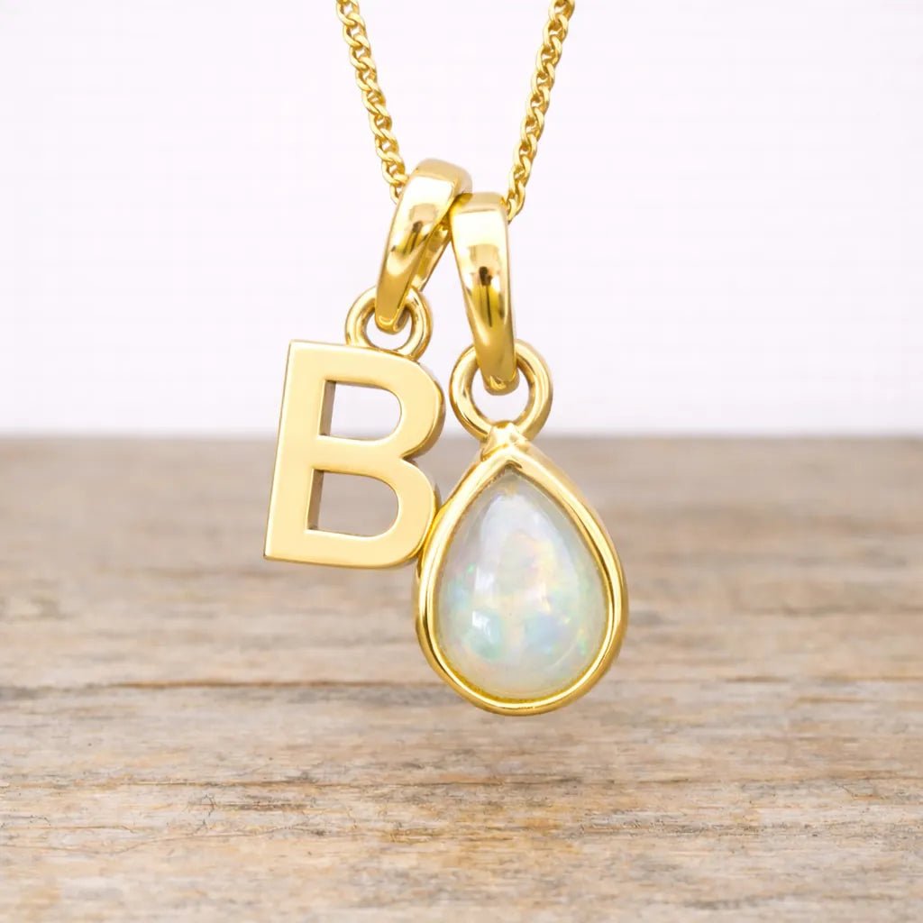 Gold necklace with 'B' pendant and teardrop-shaped pearl on a wooden surface