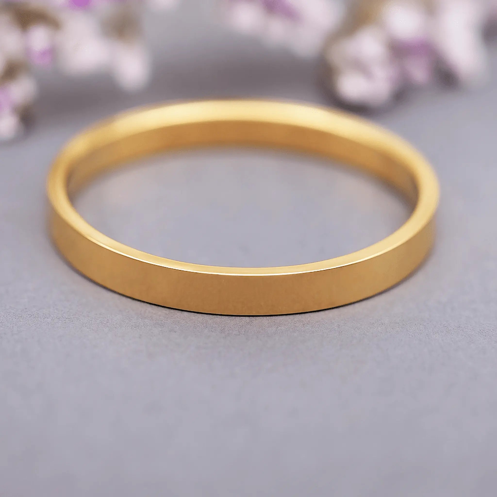 Gold band ring on a grey surface with blurred floral background