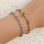 Two beaded bracelets on a person's wrist, featuring gray labradorite beads with gold spacer beads and a small oval pink stone charm, alongside peach and gray beads with gold accents.