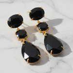 Black teardrop earrings with gold accents on a wooden surface
