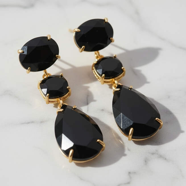 Black teardrop earrings with gold accents on a wooden surface