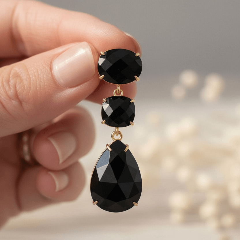 Black teardrop earrings held by a hand with a blurred background