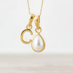 Gold necklace with a 'C' pendant and teardrop-shaped pearl on a light background