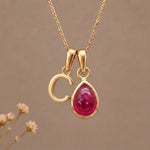 Gold Initial C Pendant and July birthstone Natural Ruby Necklace against a warm background