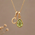Gold Initial C Pendant and August birthstone Natural Peridot Necklace against a warm background