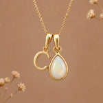Gold Initial C Pendant and October birthstone Natural Opal Necklace against a warm background