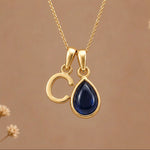 Gold Initial C Pendant and September birthstone Natural Sapphire Necklace against a warm background