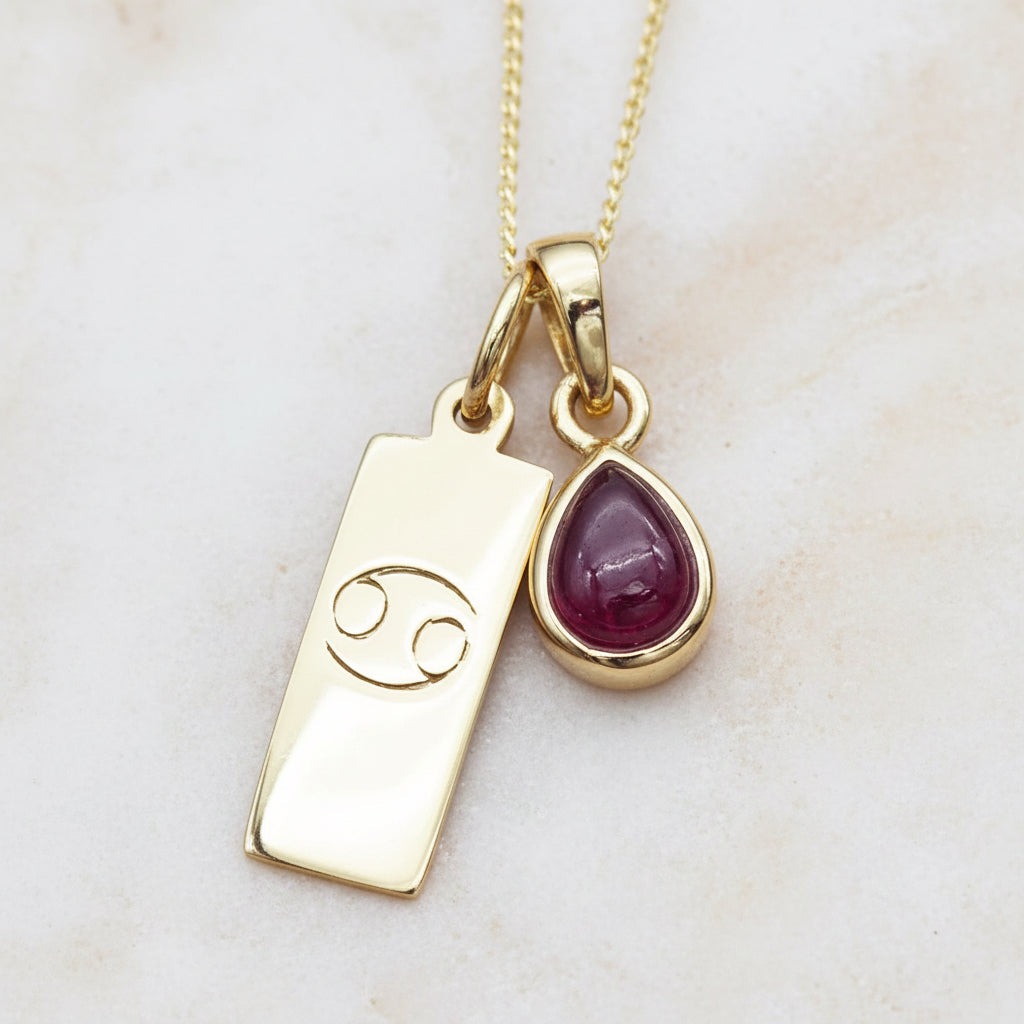 gold chain with a gold Zodiac Cancer symbol pendant and gold ruby pendant on a organic background